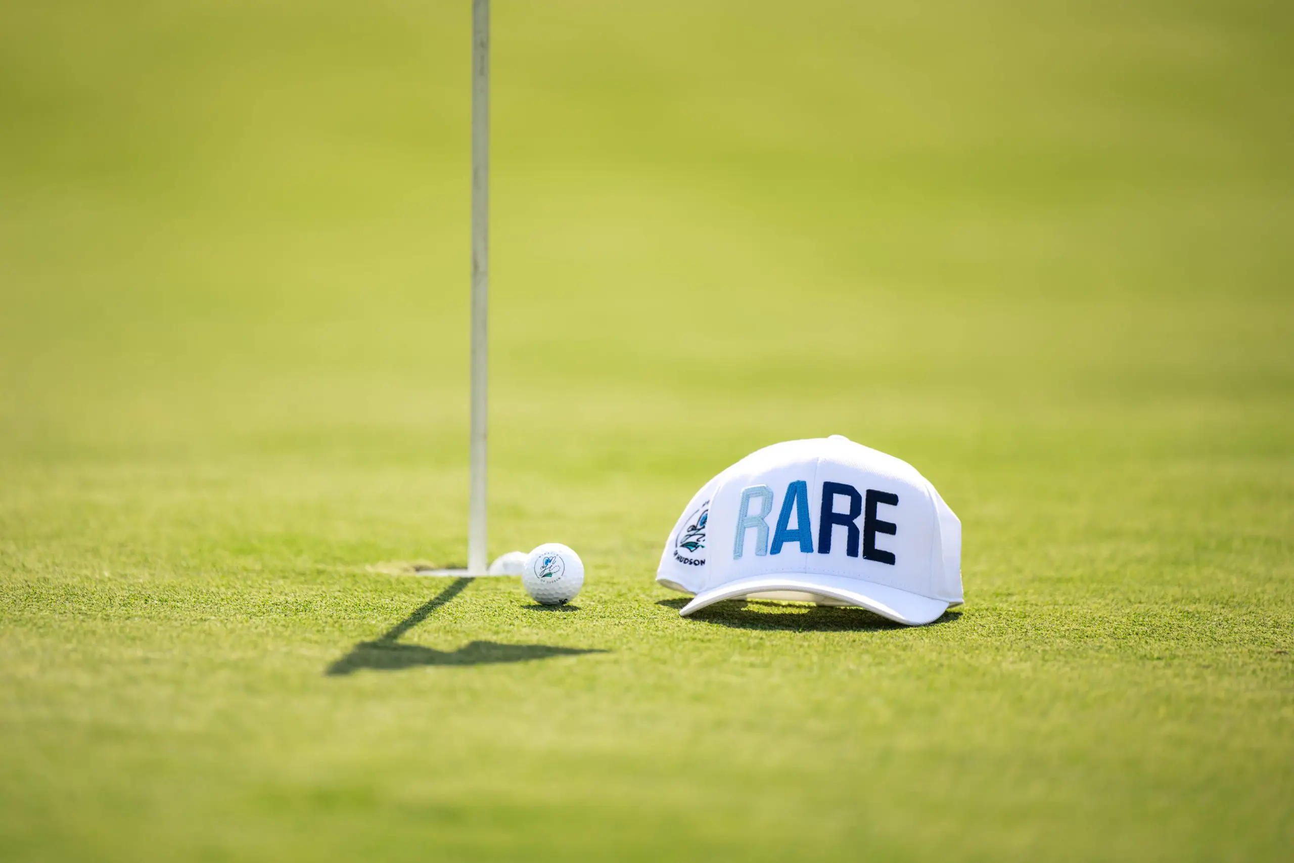 Golf ball and hat close-up on green during a nonprofit charity event with video and photography coverage.