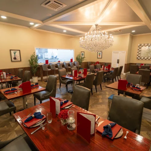 Spacious dining area with modern furnishings, a large crystal chandelier, warm neutral tones, and an open kitchen view designed to highlight elegance and ambiance.